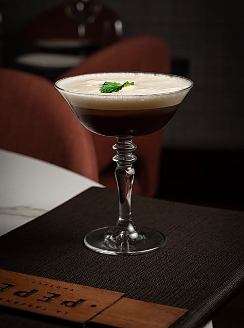 Espresso martini en copa de cristal con espuma y hoja de menta