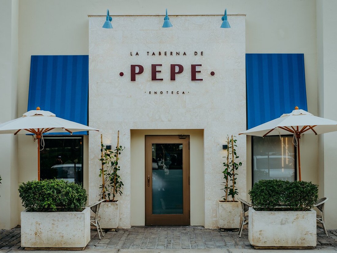 Fachada de La Taberna de Pepe con el rótulo de la marca, toldos azules y sombrillas