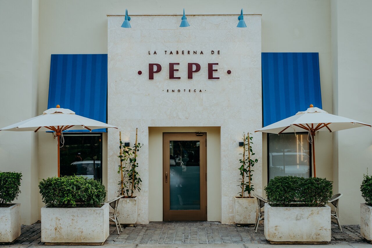 Fachada de La Taberna de Pepe en Punta Cana Village, con el rótulo de la marca pintado en la pared, toldos azules y sombrillas blancas
