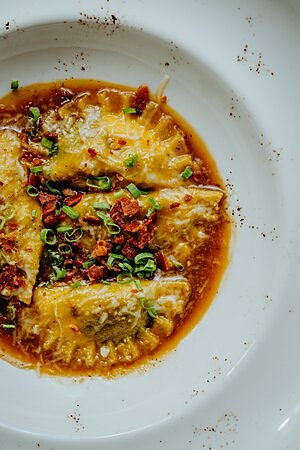 Ravioli de cochinillo gratinado con salsa sobre plato blanco