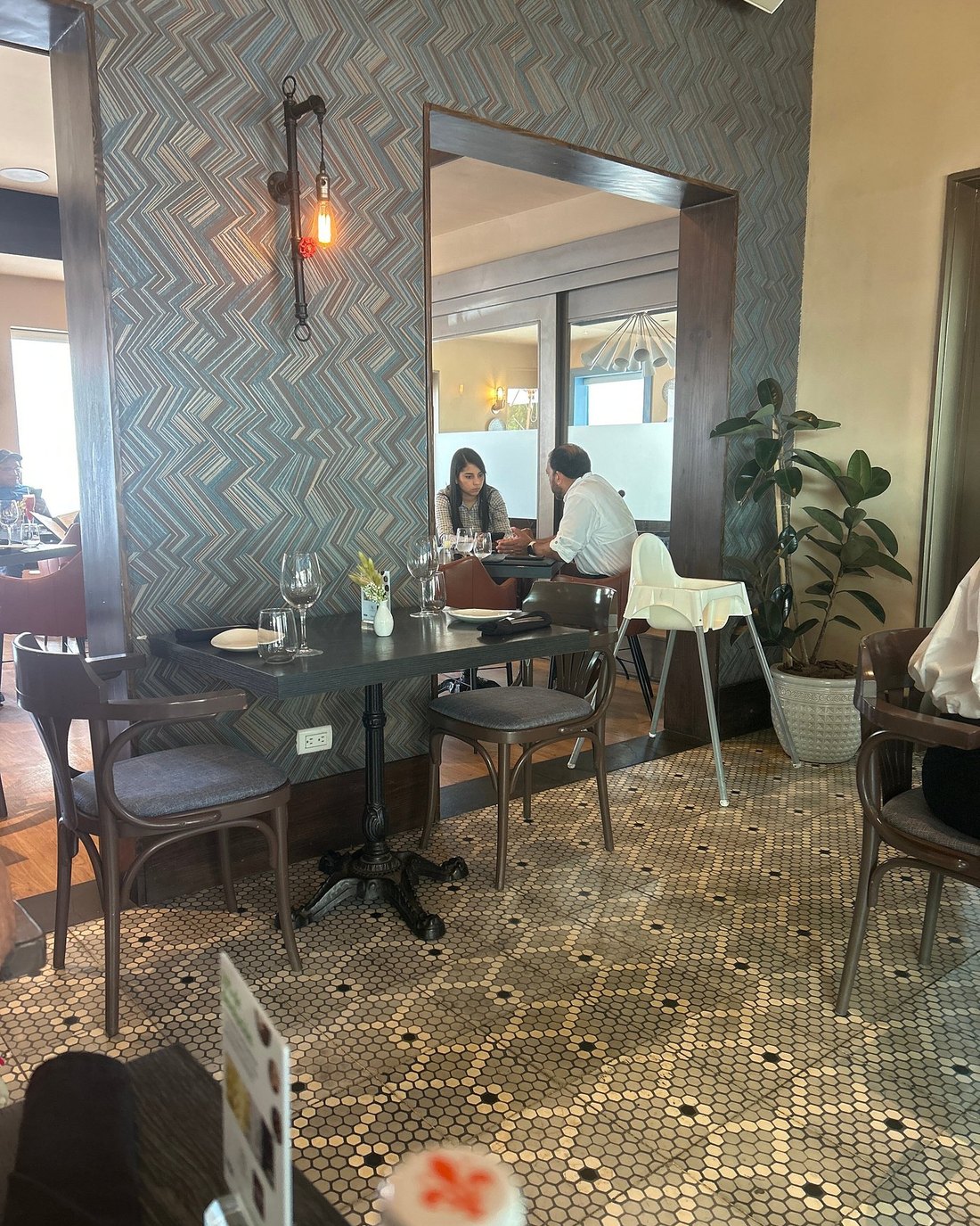Salón de La Taberna de Pepe con papel tapiz geométrico, aplique de pared, mesas vestidas y comensales